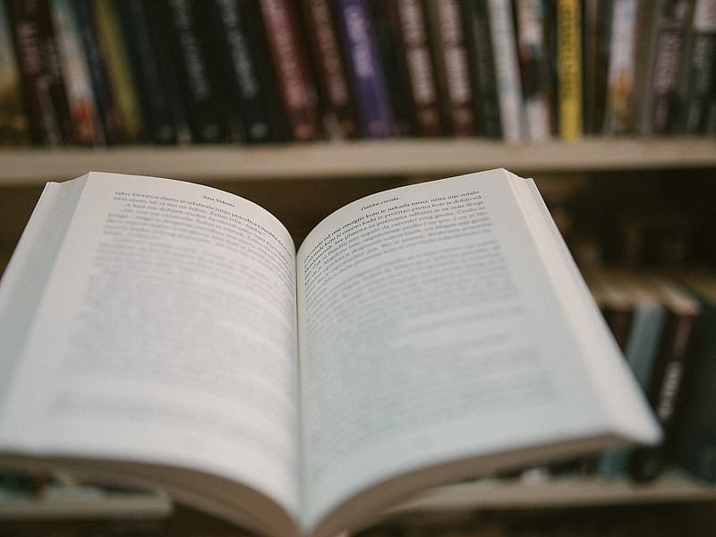 An open book on a table in front of library shelves
