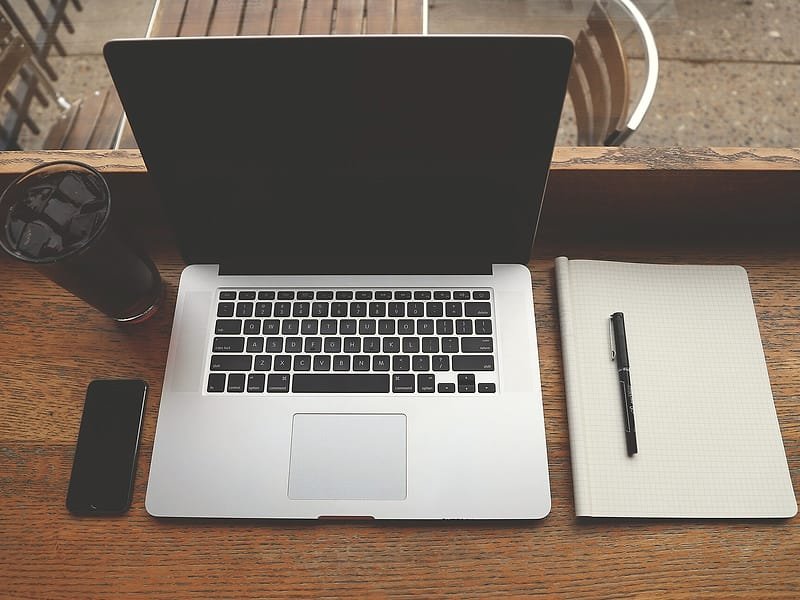 A laptop, notebook, phone and coffee on a wooden desk, seen from above