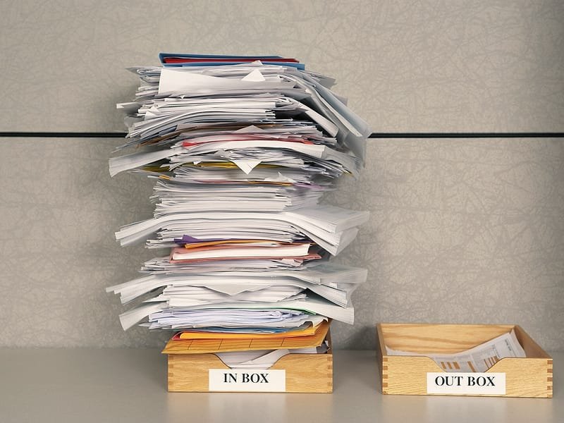 A tall stack of papers in an in-tray next to an out-tray